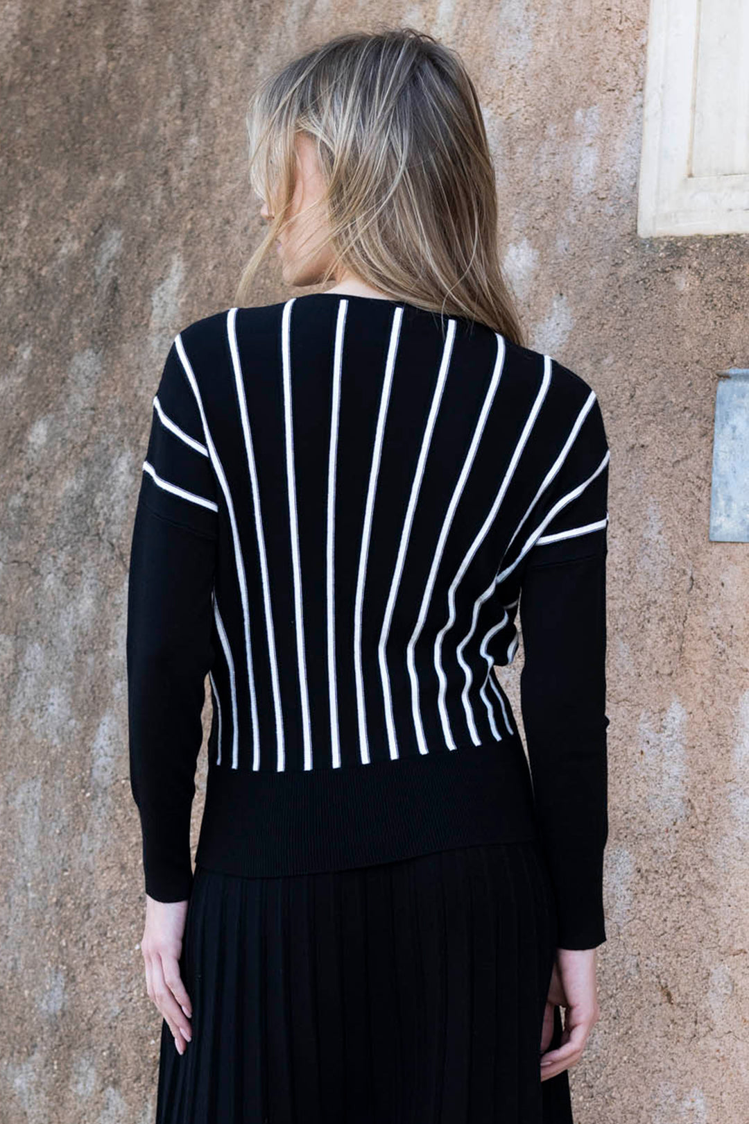 Person wearing a black and white striped sweater against a textured wall.