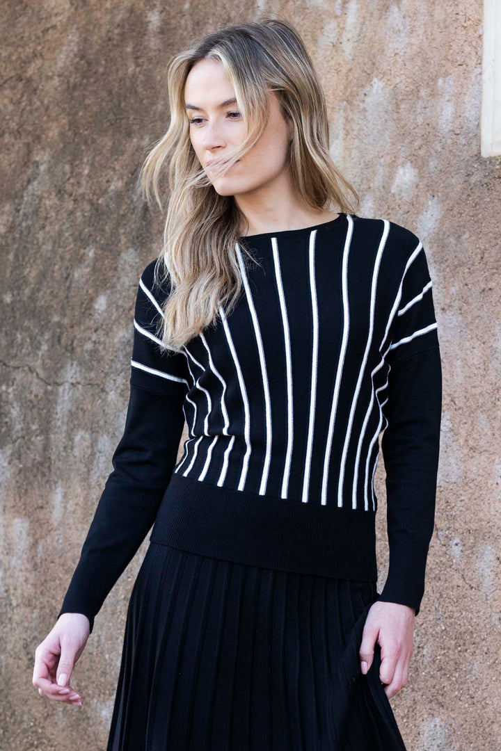 Woman wearing a black and white striped sweater against a textured wall.