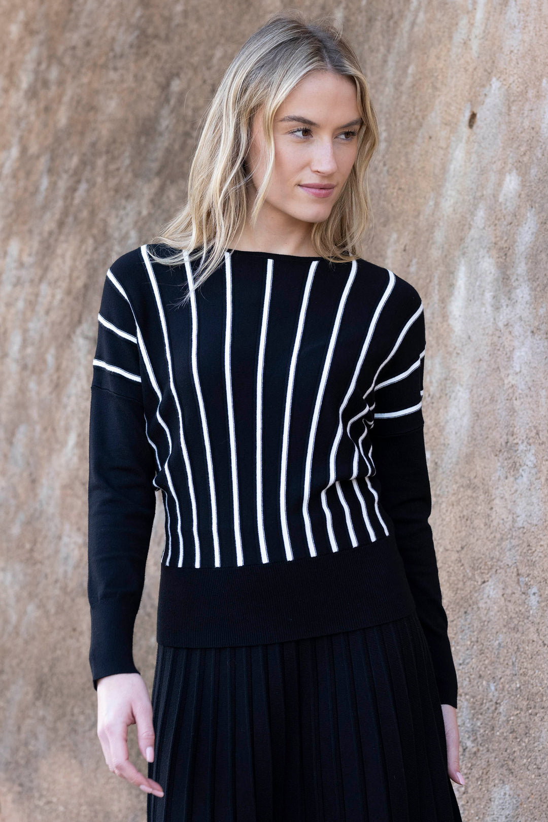 Woman wearing a black sweater with white stripes against a beige wall
