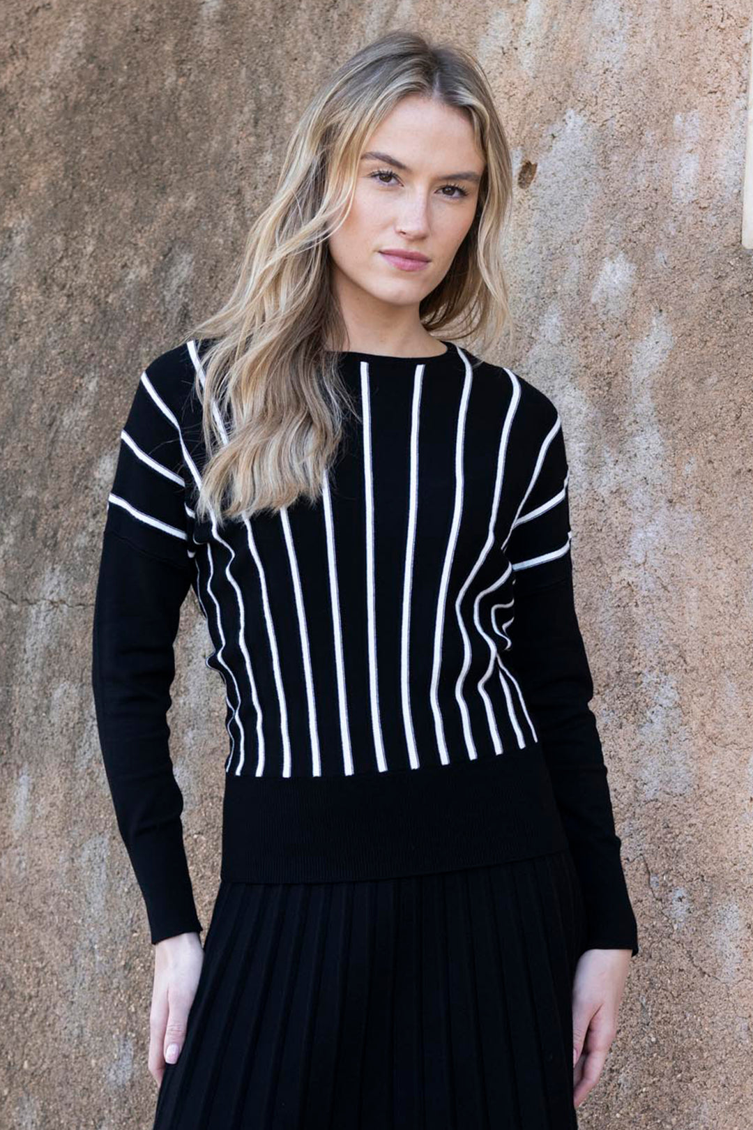 Woman wearing a black and white striped sweater against a textured beige wall