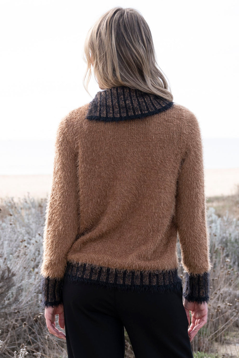 Person wearing a brown sweater with a patterned collar in an outdoor setting