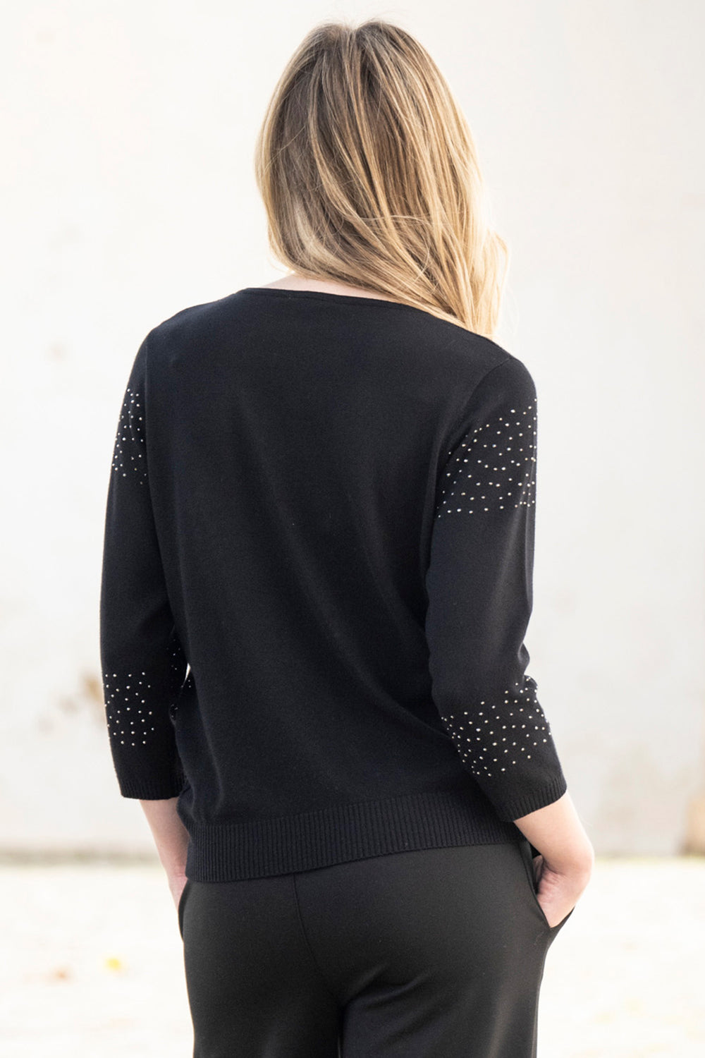 Black sweater with embellished sleeves worn by a person on a light background