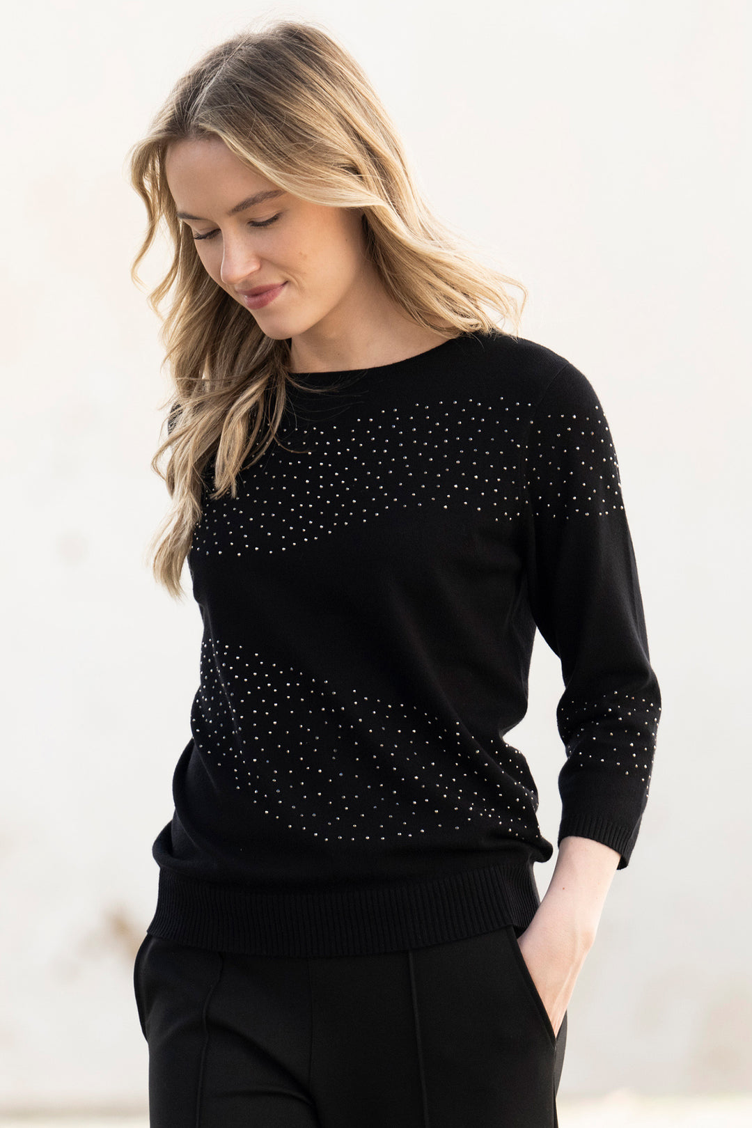 Woman wearing a black sweater with small embellishments on a light background