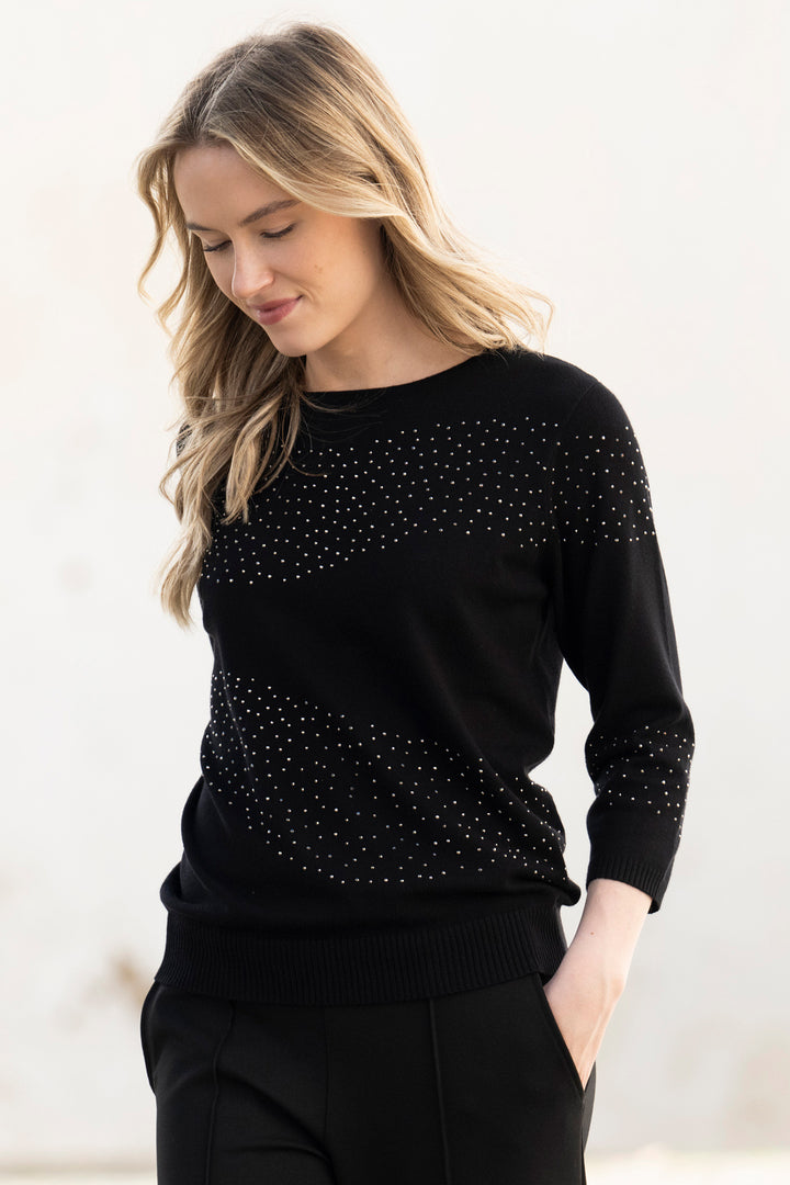Woman wearing a black sweater with small embellishments on a light background