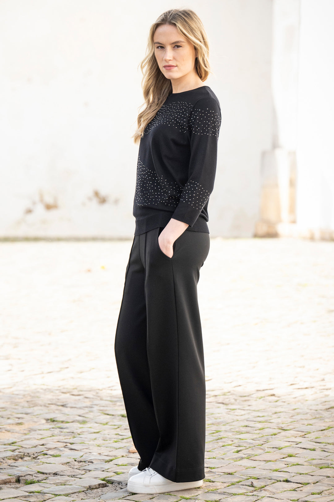 Woman wearing a black outfit with a patterned top and wide-leg pants on a light background