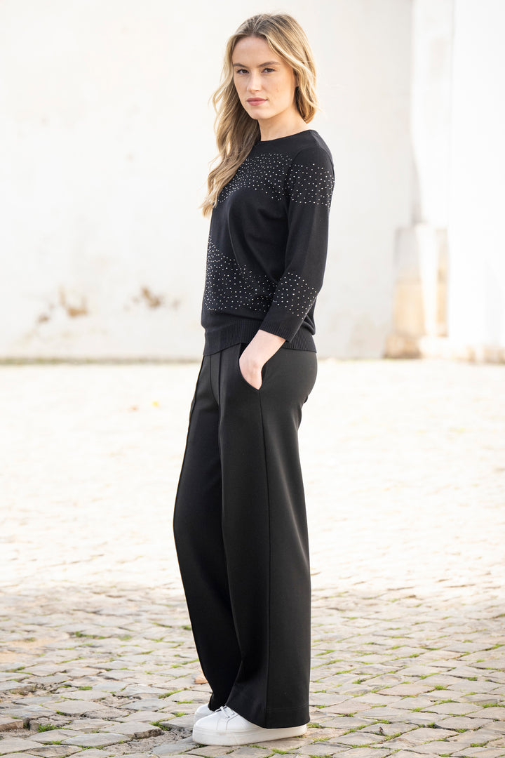 Woman wearing a black outfit with a patterned top and wide-leg pants on a light background