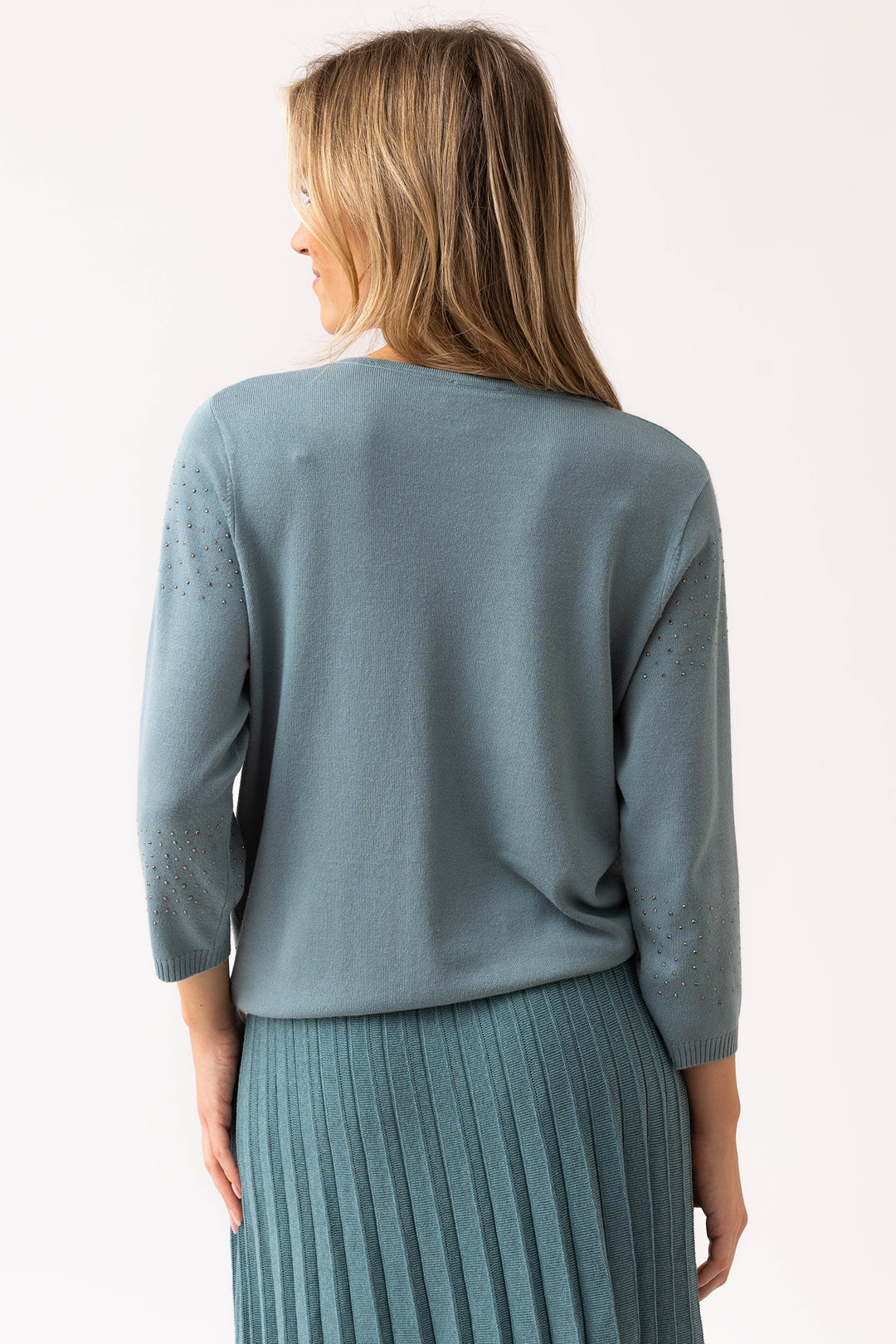 Woman wearing a light blue sweater and pleated skirt against a white background