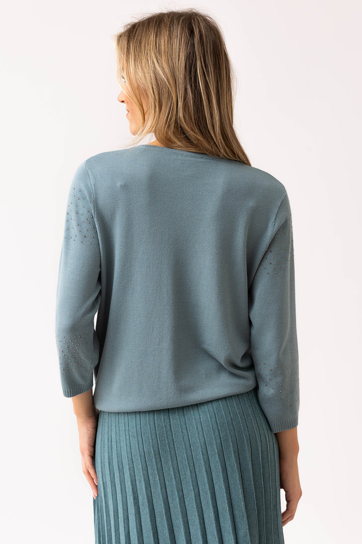 Woman wearing a light blue sweater and pleated skirt against a white background