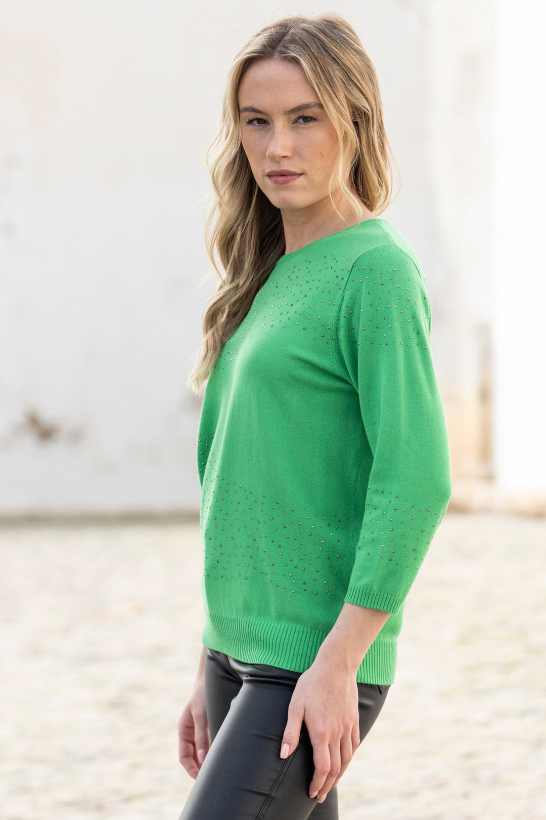 Woman wearing a green sweater standing on a sandy surface with a blurred background