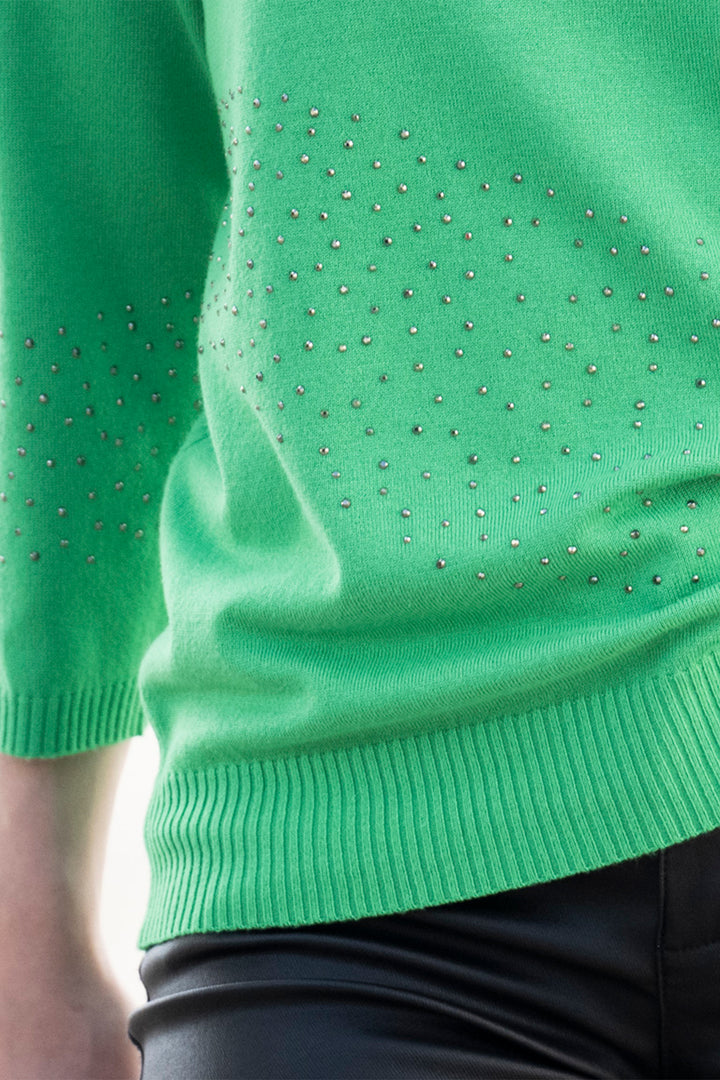 Green sweater with rhinestone embellishments on a blurred background