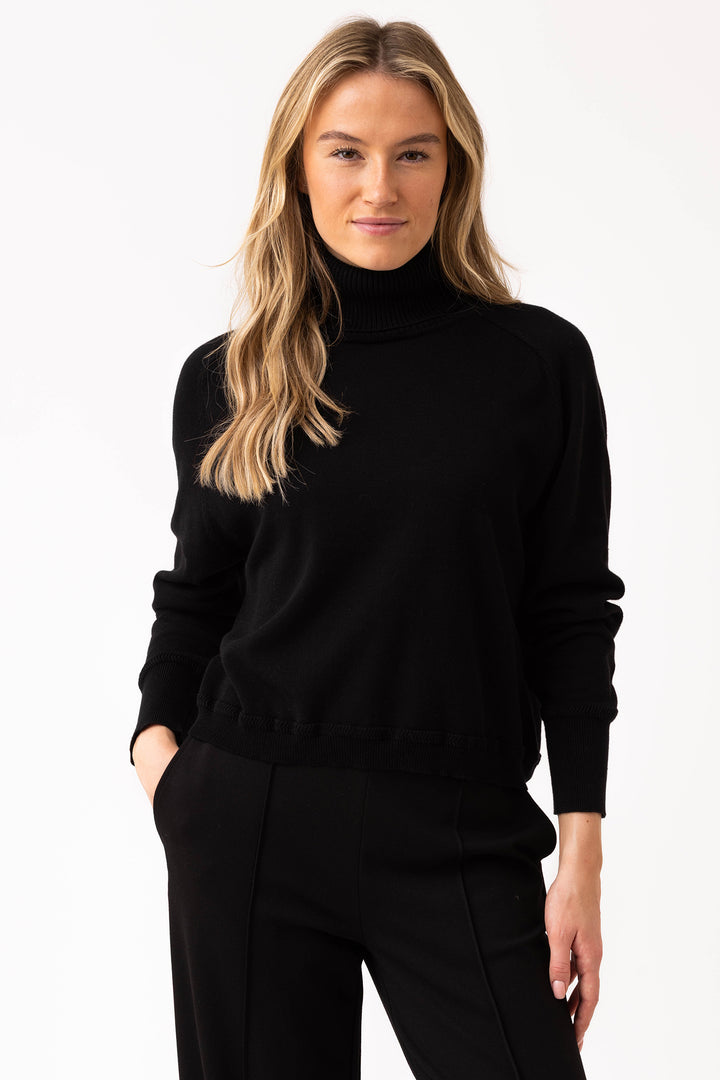 Woman wearing a black turtleneck sweater and black pants on a white background