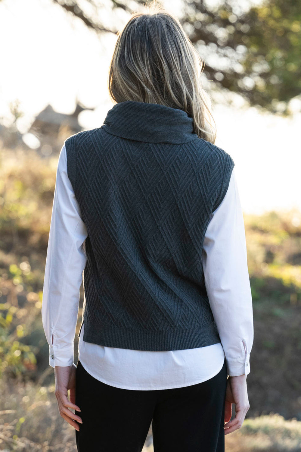 Person wearing a dark green knitted vest over a white shirt outdoors.