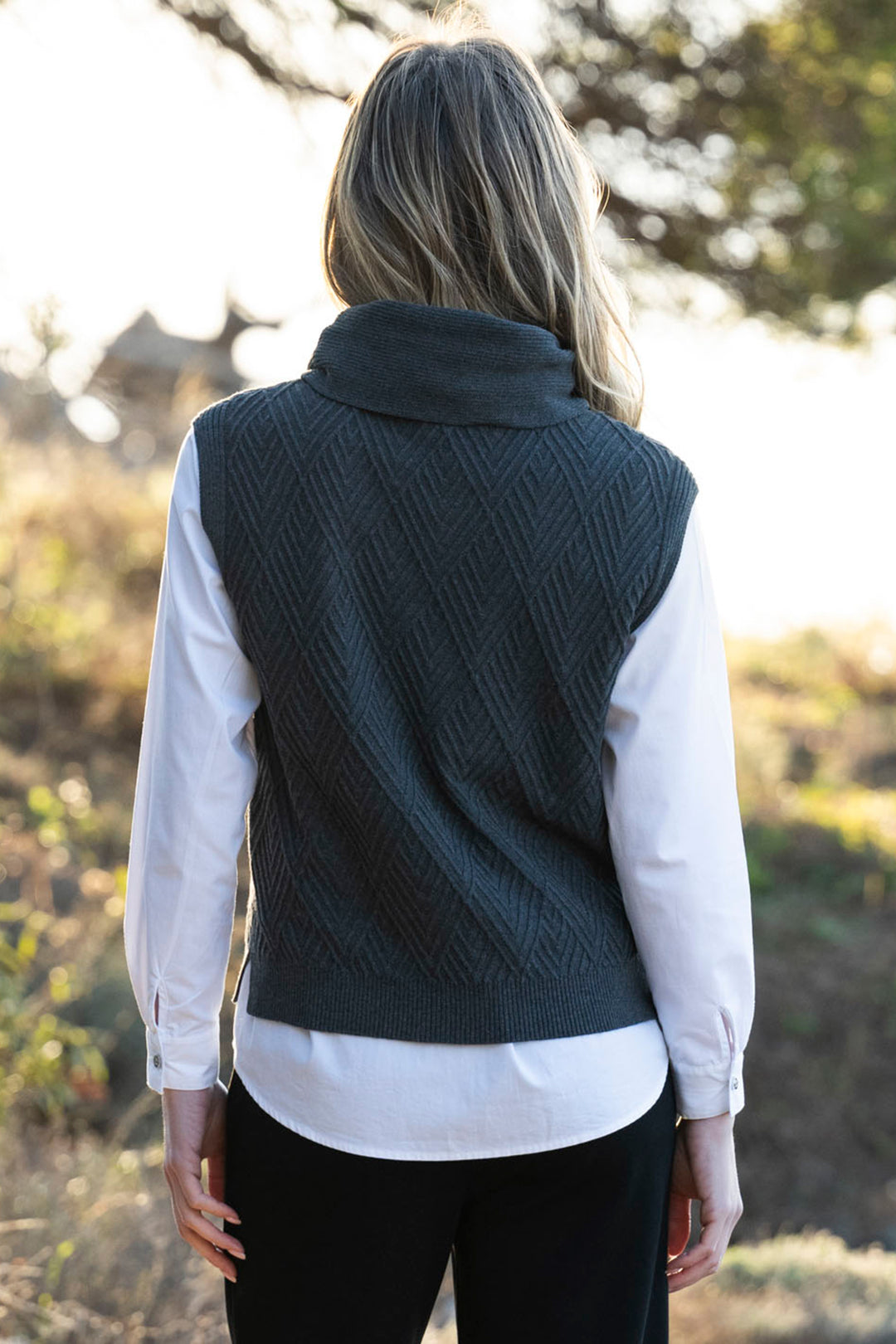 Person wearing a dark green knitted vest over a white shirt outdoors.
