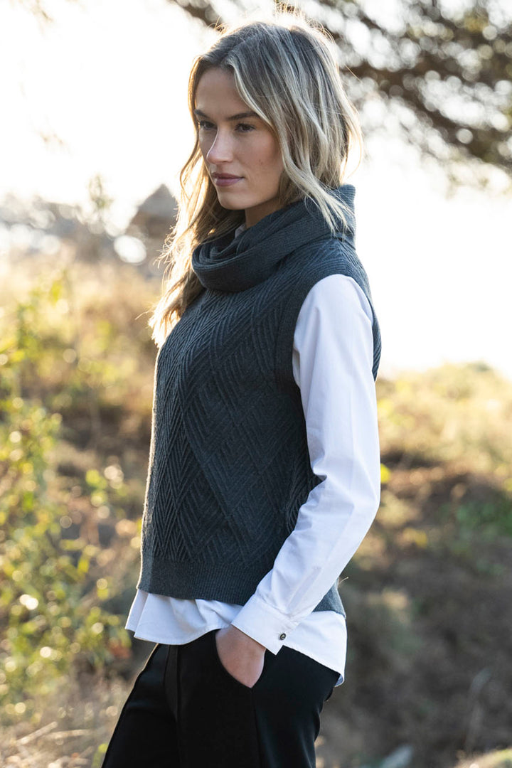 Woman wearing a dark green knitted vest over a white shirt in an outdoor setting.
