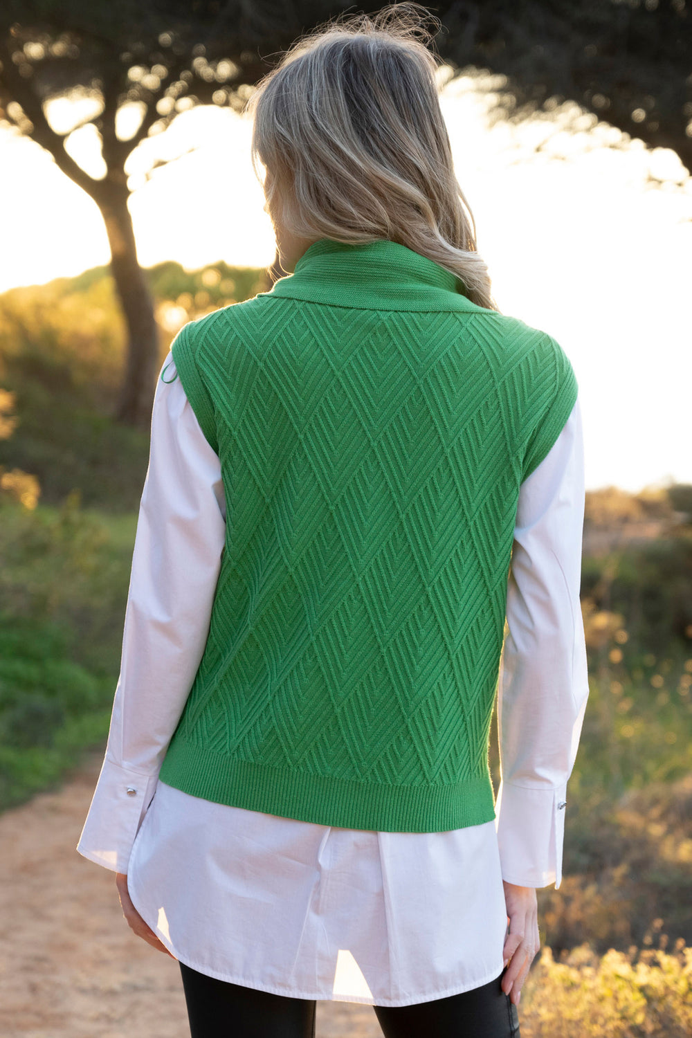 Person wearing a green knitted vest over a white shirt outdoors.