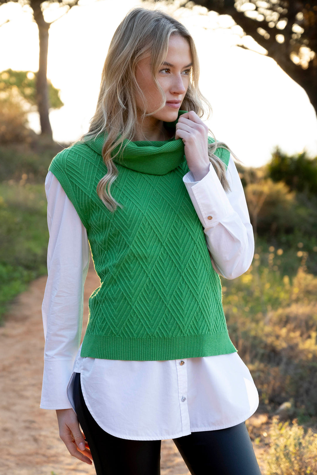 Woman wearing a green knitted vest over a white shirt outdoors.