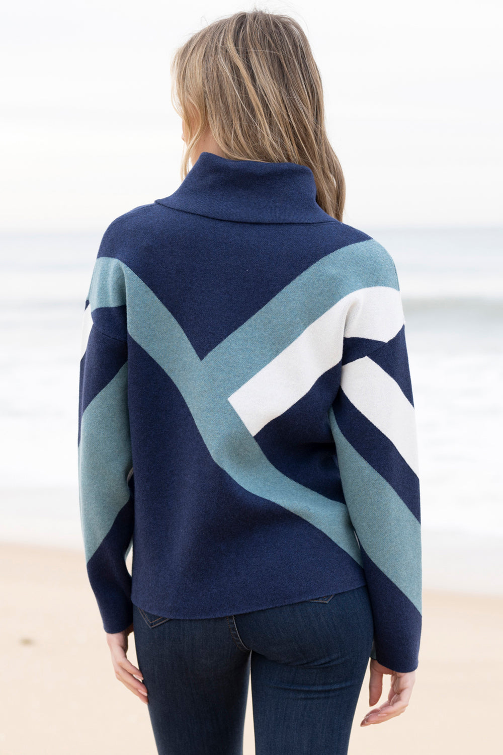 Person wearing a blue, green, and white patterned sweater on a beach.