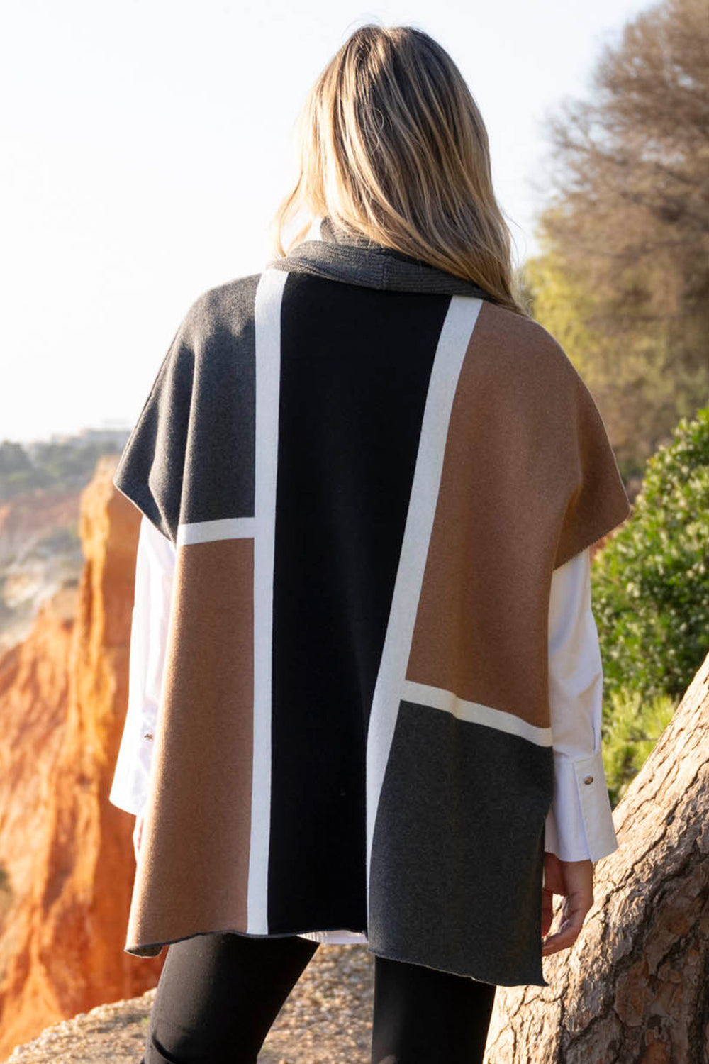 Person wearing a patterned coat standing outdoors with trees and rocks in the background