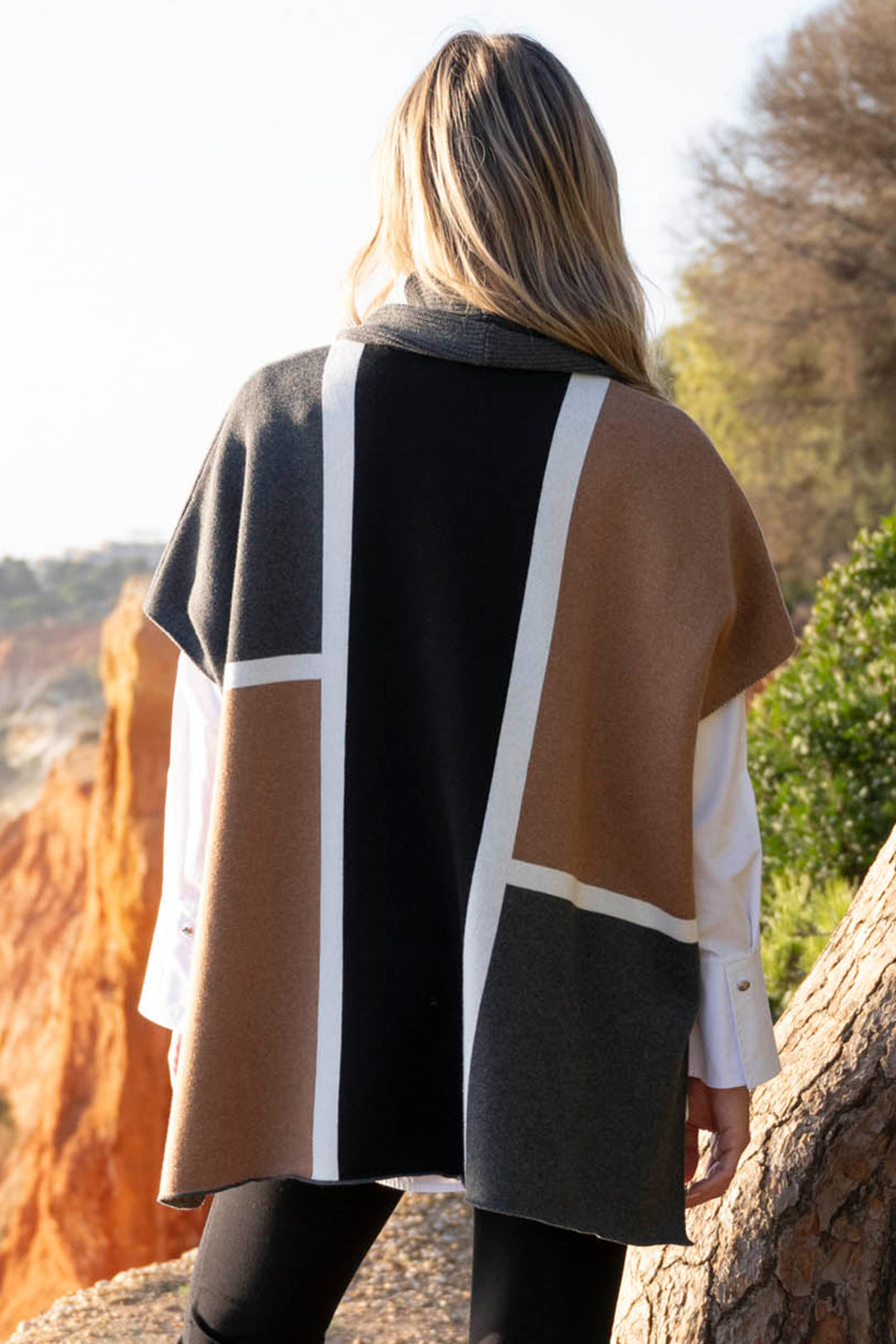 Person wearing a patterned coat standing outdoors with trees and rocks in the background
