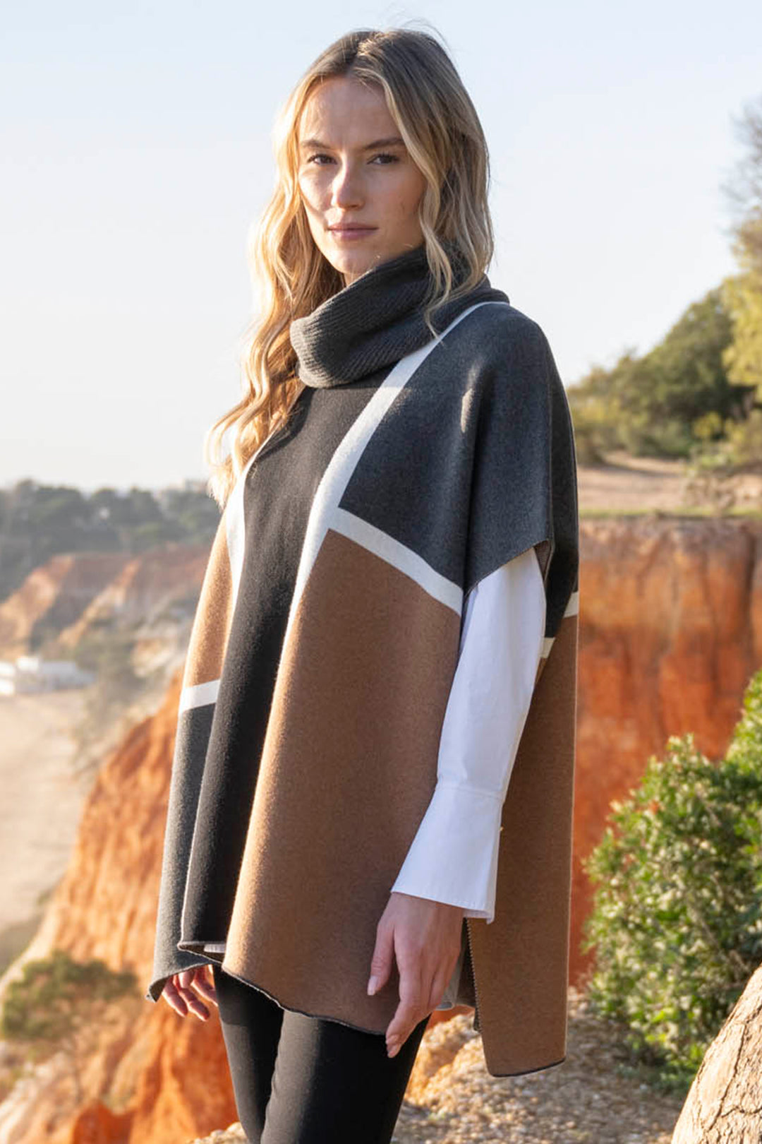 Woman wearing a color-blocked poncho outdoors with a scenic background