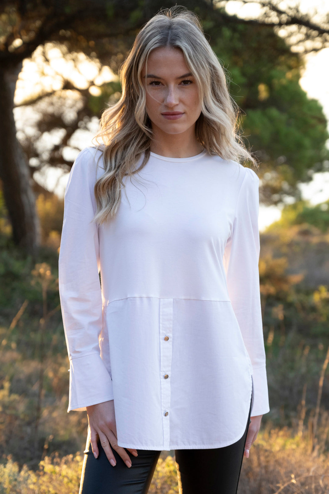 Woman wearing a white long-sleeve top outdoors with trees in the background