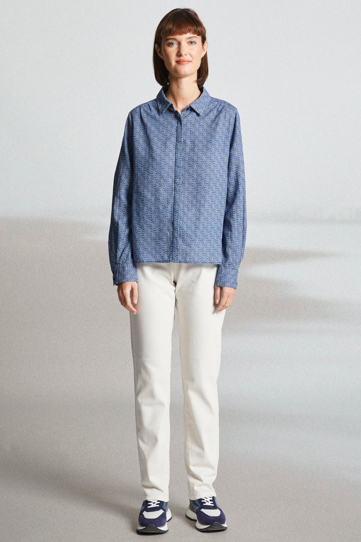 Person wearing a blue patterned shirt and white pants on a plain background