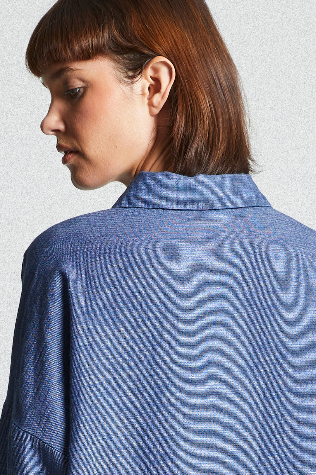 Person wearing a blue denim shirt against a plain background