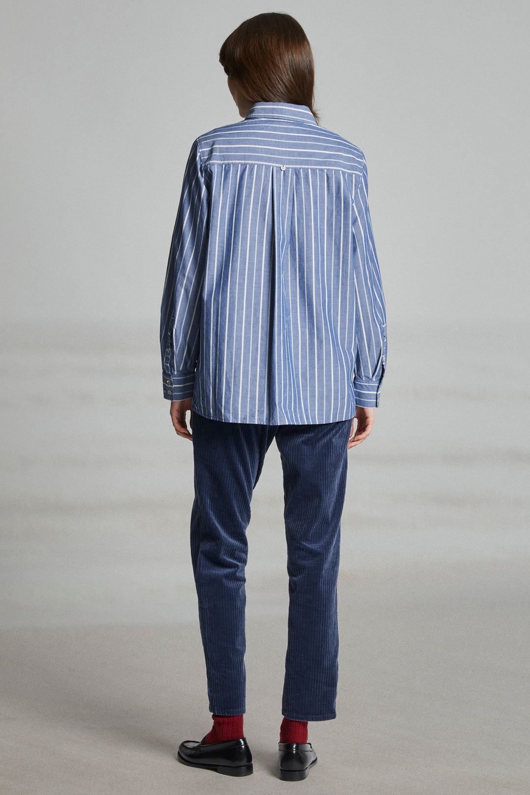 Person wearing a blue striped shirt and dark pants on a plain background