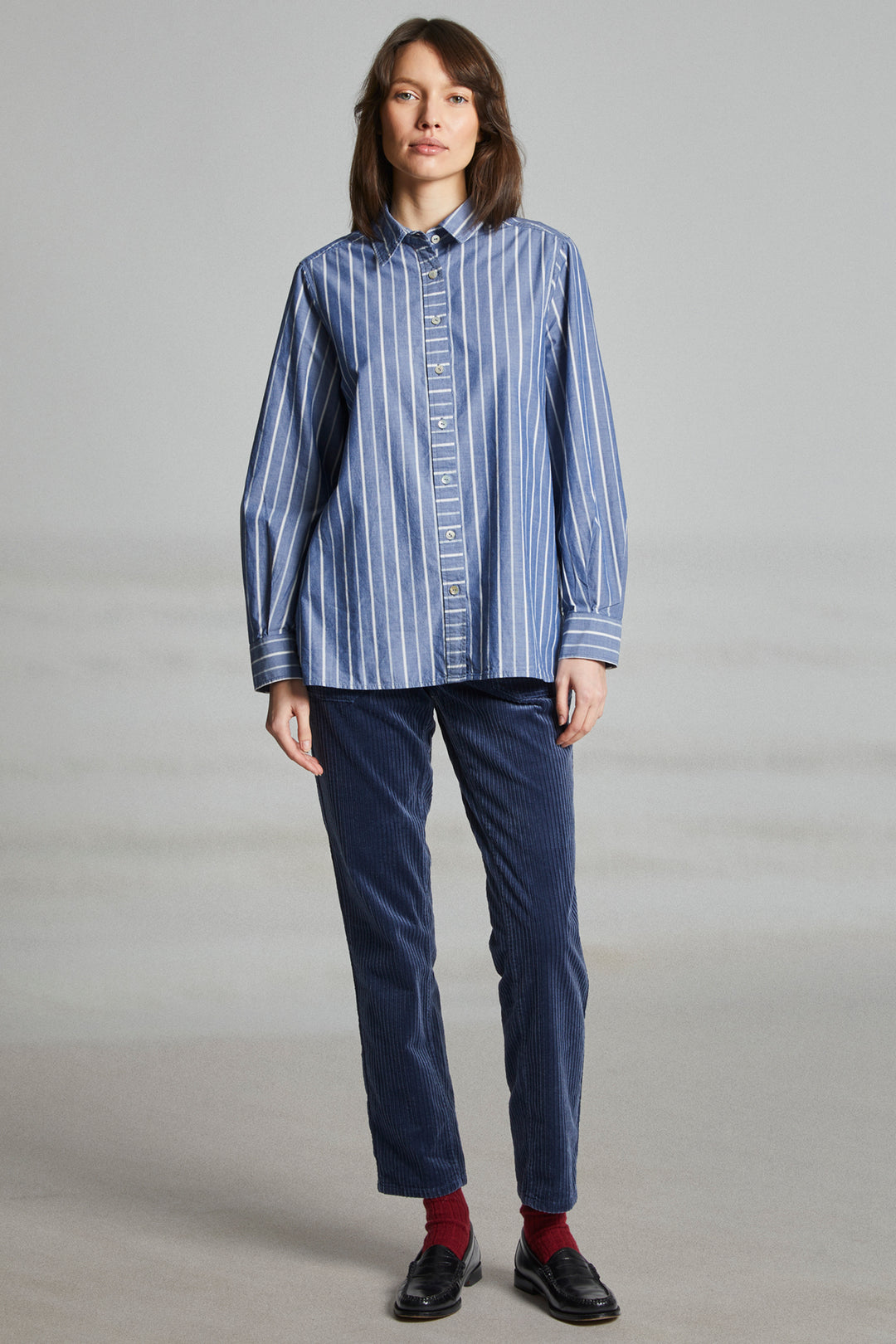 Person wearing a blue striped shirt and dark pants on a gray background