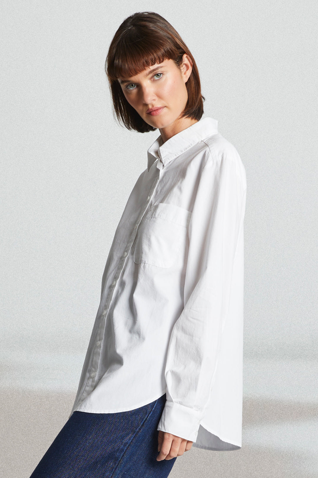 Woman wearing a white shirt and blue jeans against a plain background