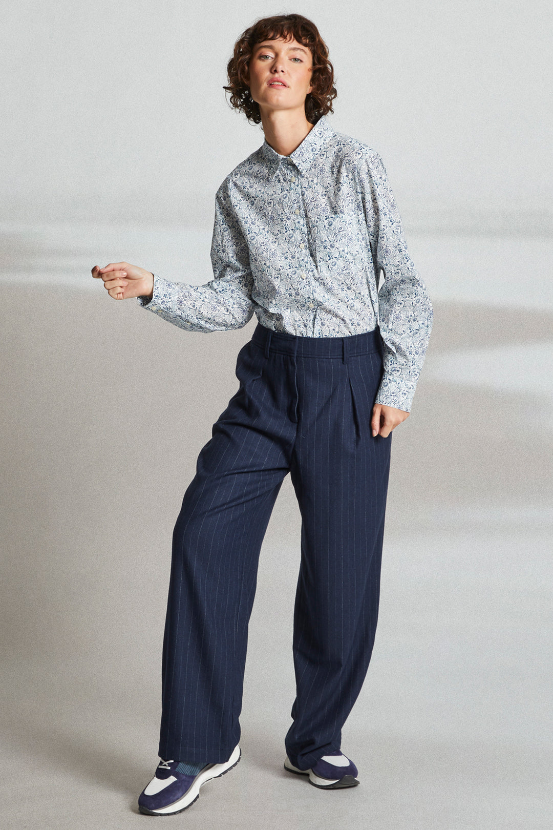 Person wearing a light patterned shirt and dark pants on a plain background