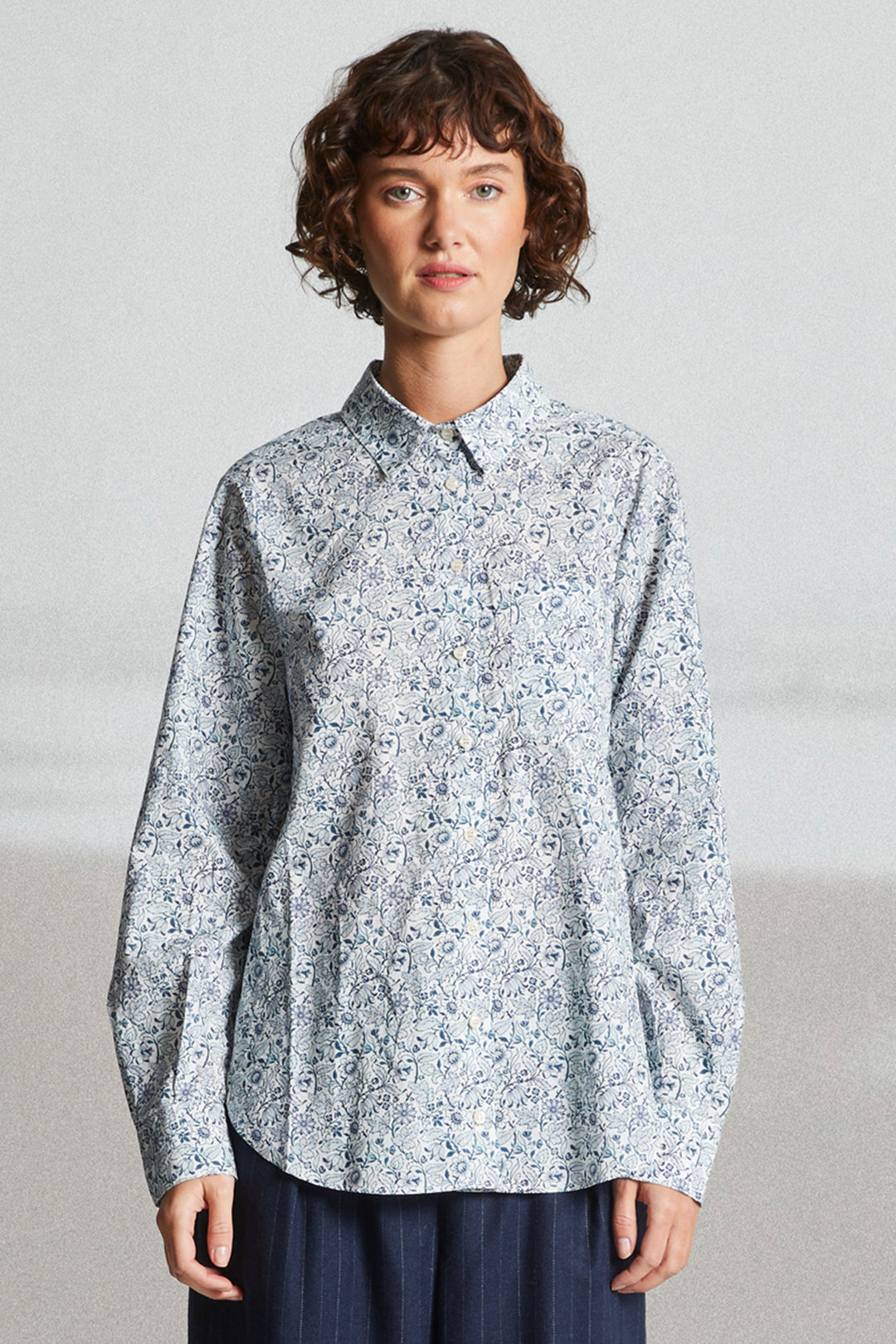 Person wearing a light blue floral patterned shirt against a plain background