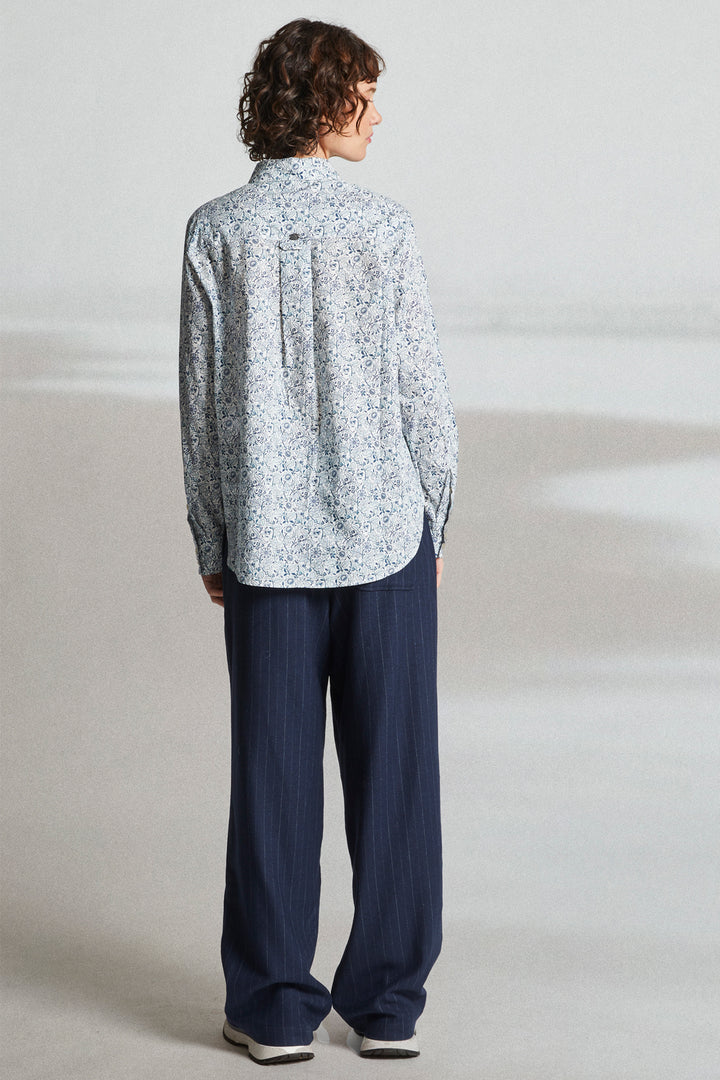 Person wearing a light patterned shirt and dark pants on a plain background