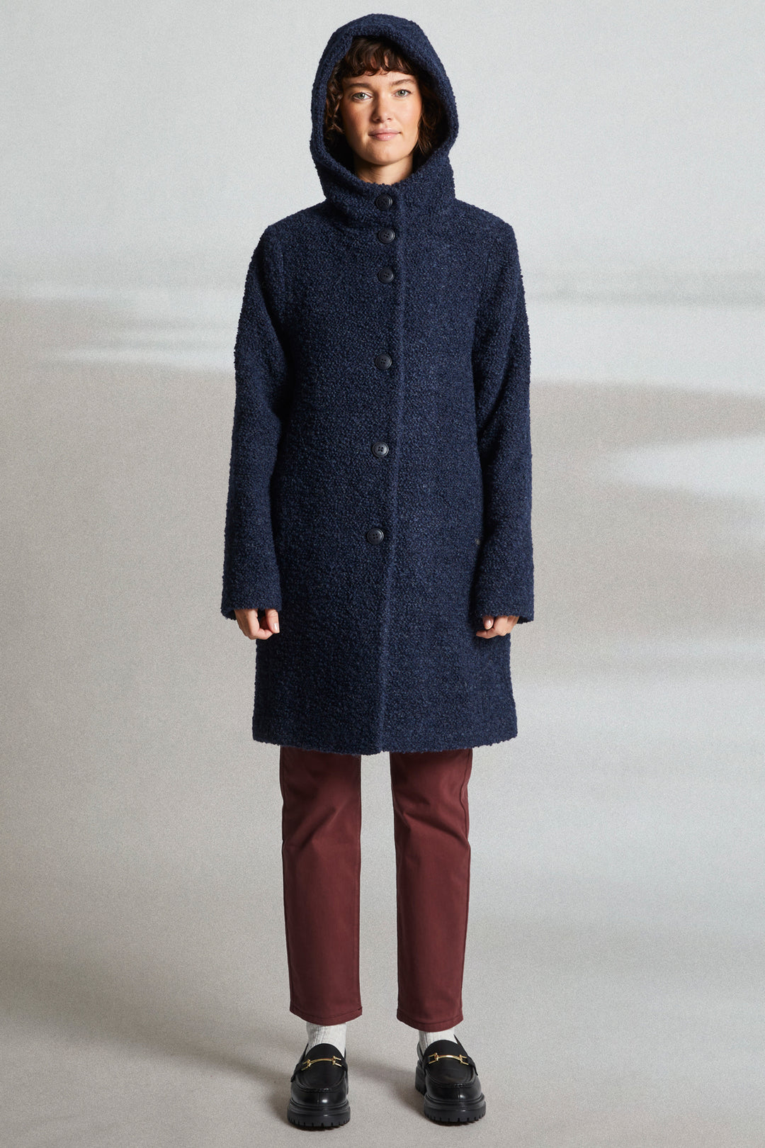 Person wearing a long navy coat with a hood on a plain background