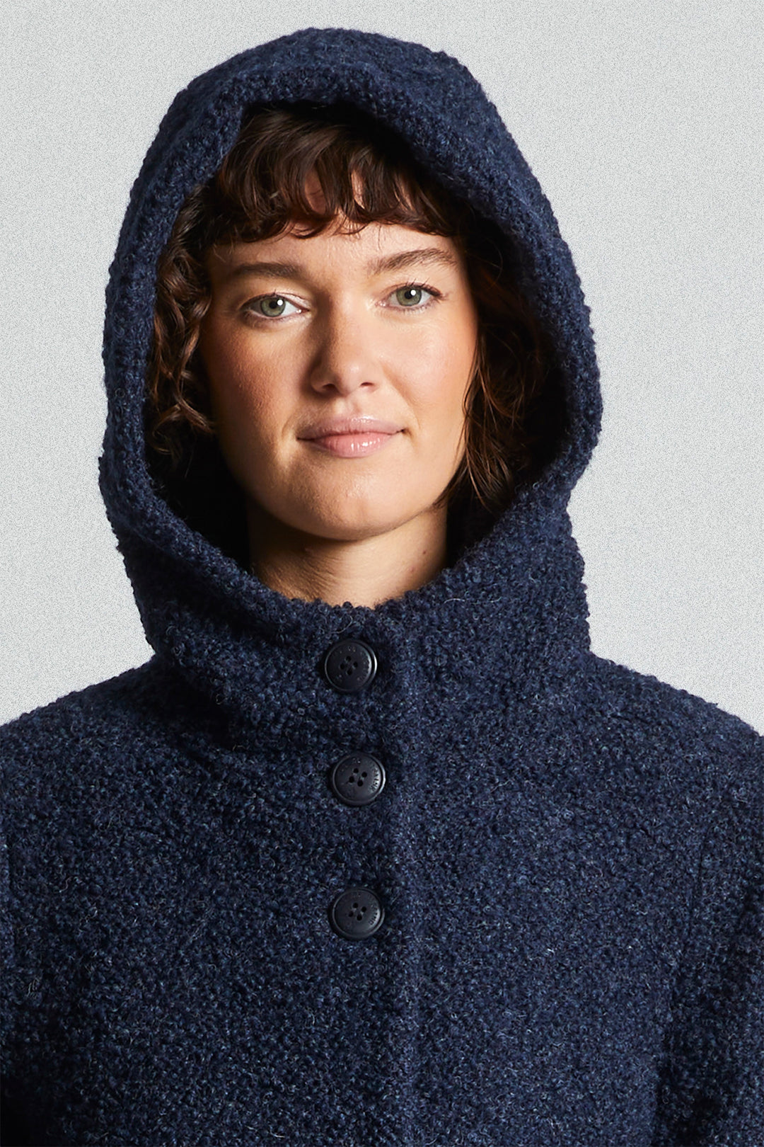 Person wearing a dark blue hooded coat with buttons on a light gray background