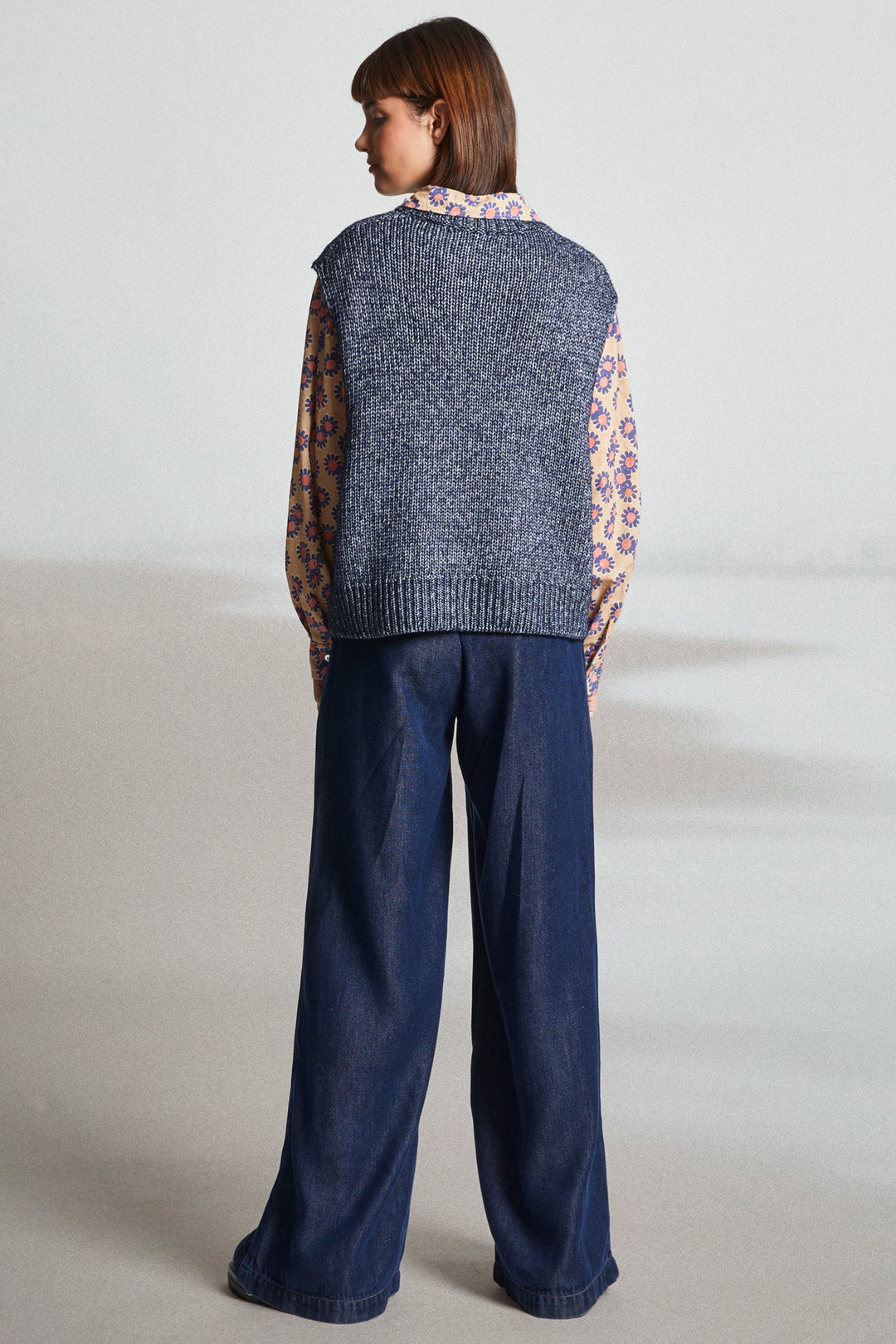 Person wearing a blue knitted vest and dark blue pants on a plain background