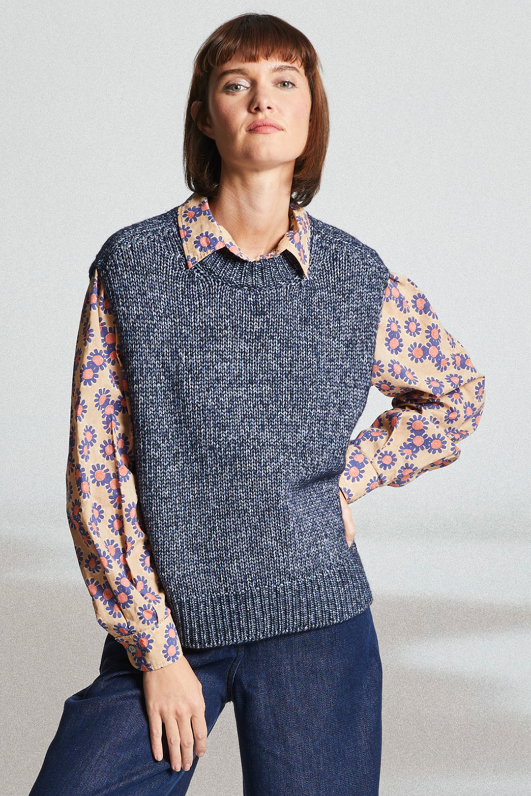 Woman wearing a gray knitted vest over a floral blouse with a plain background