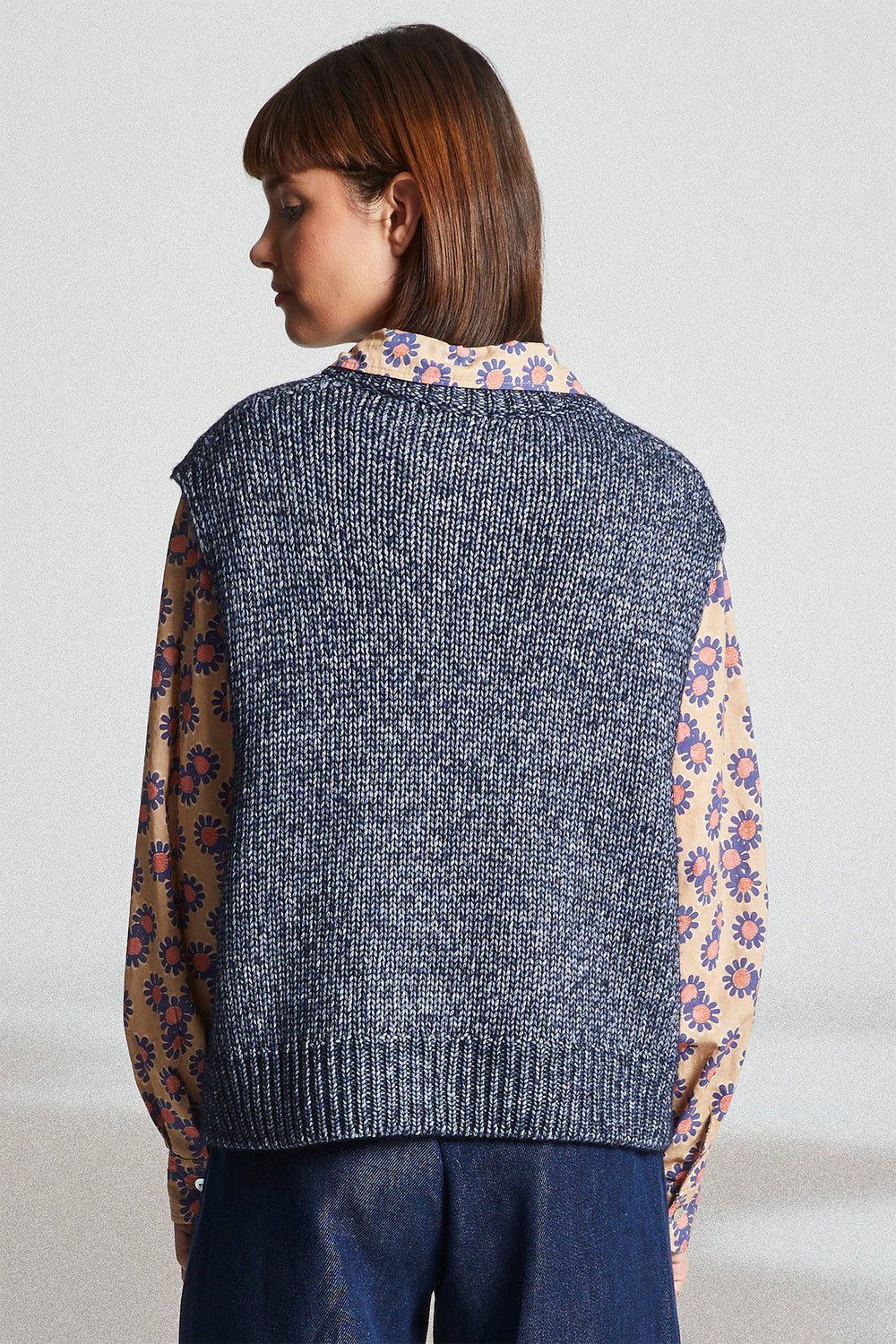 Woman wearing a gray knitted vest over a colorful floral shirt with a plain background