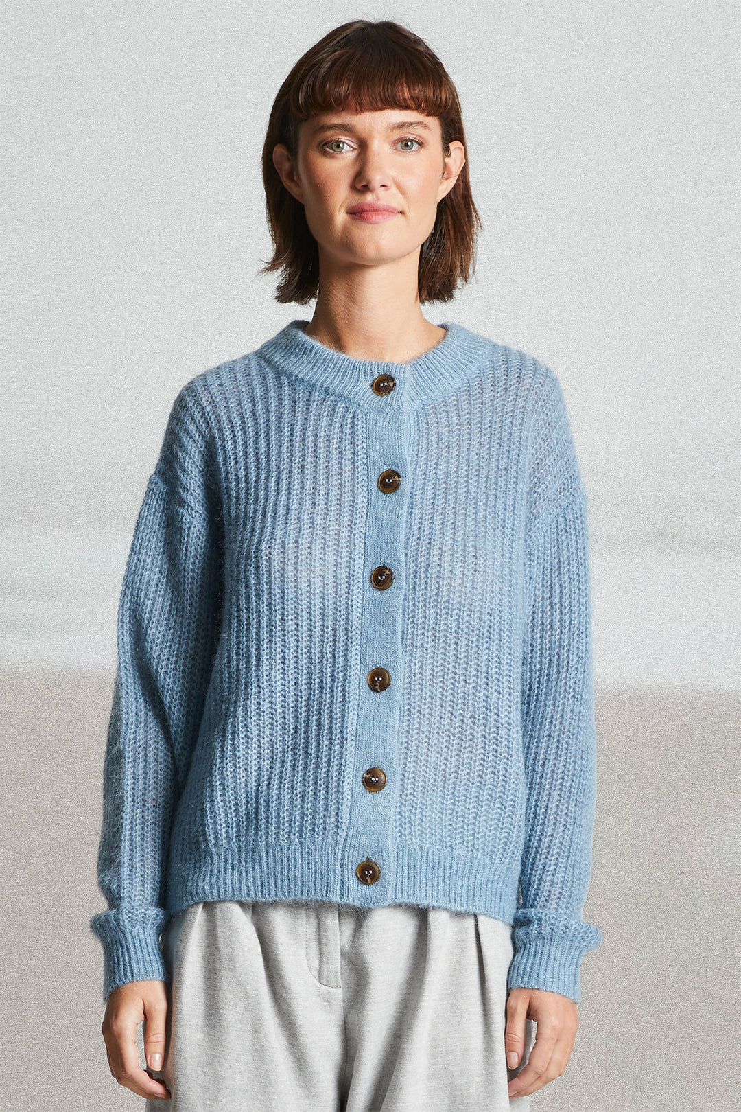 Woman wearing a blue knitted cardigan with brown buttons on a light gray background