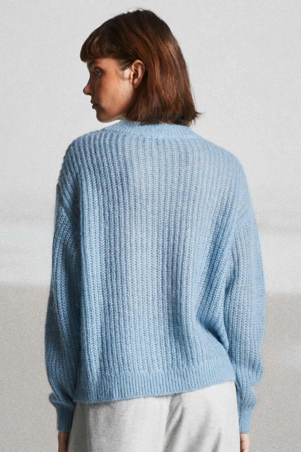 Person wearing a light blue knitted sweater against a plain background