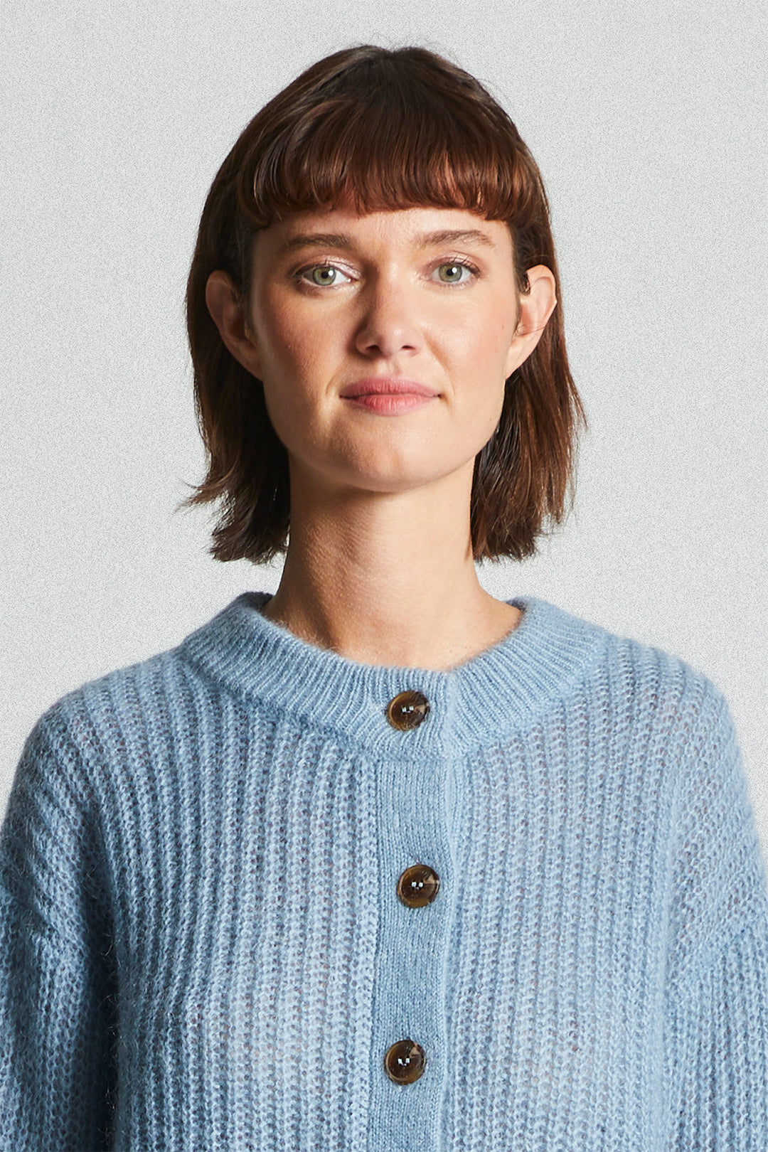 Woman wearing a light blue knitted cardigan against a plain background