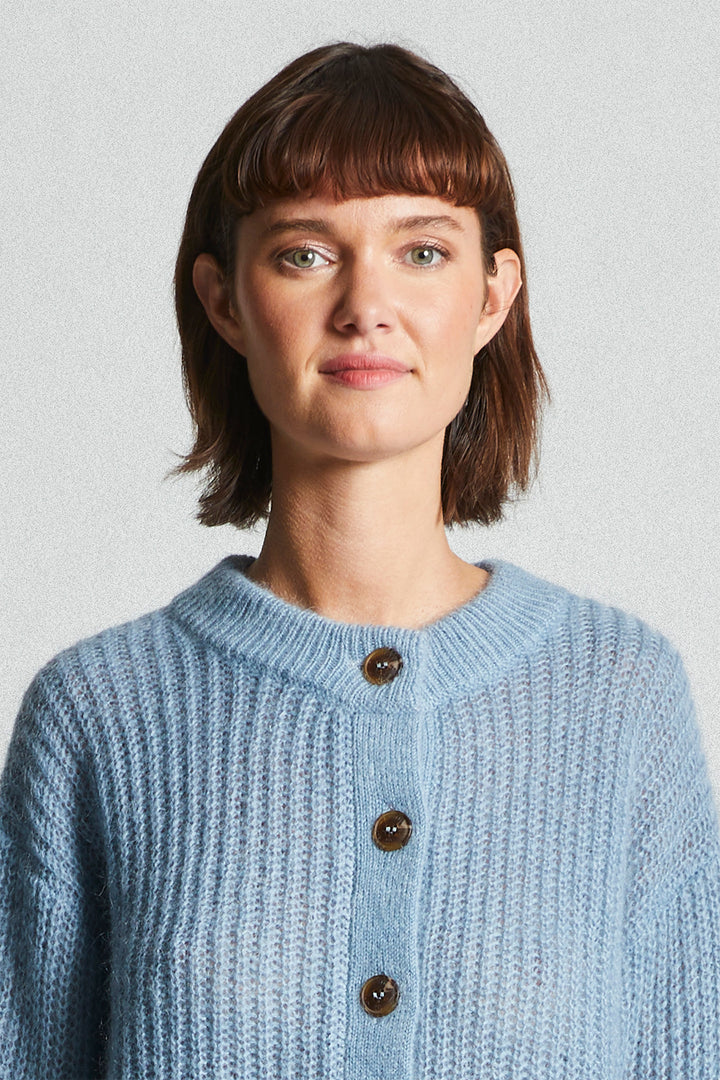 Woman wearing a light blue knitted cardigan against a plain background
