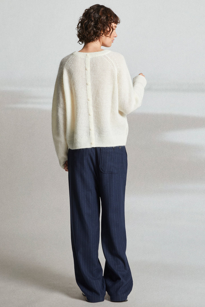 Person wearing a white sweater and navy pants on a light gray background