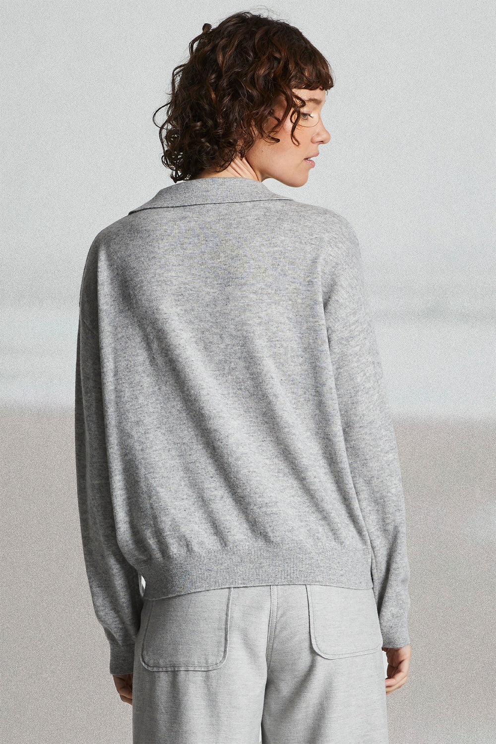 Person wearing a gray sweater and light gray pants against a plain background