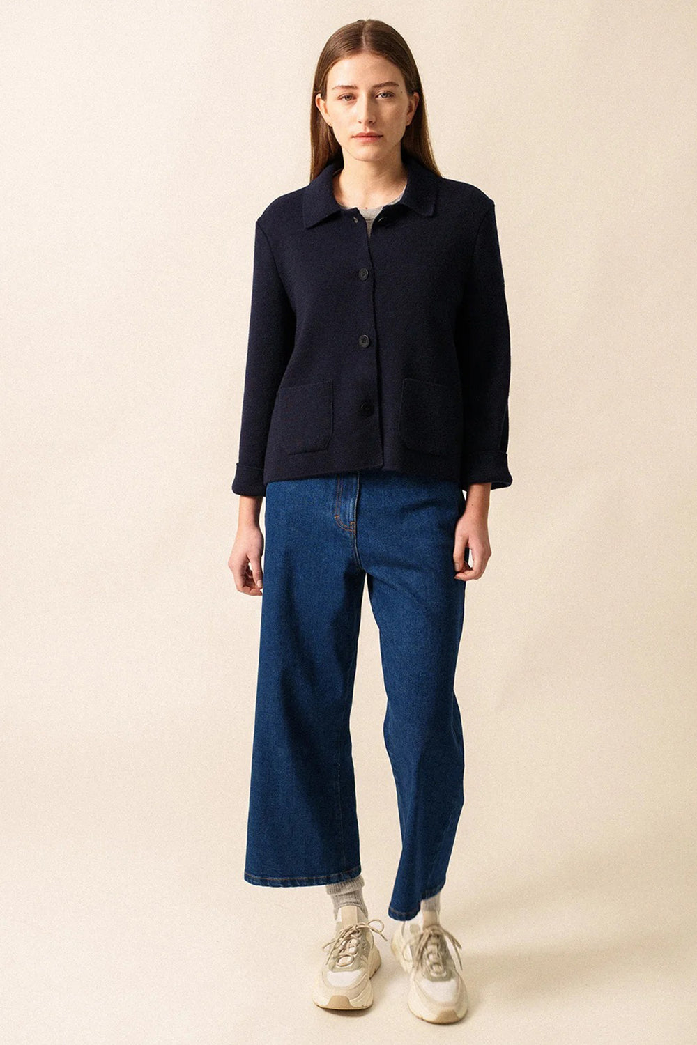 Person wearing a navy jacket and blue jeans on a beige background