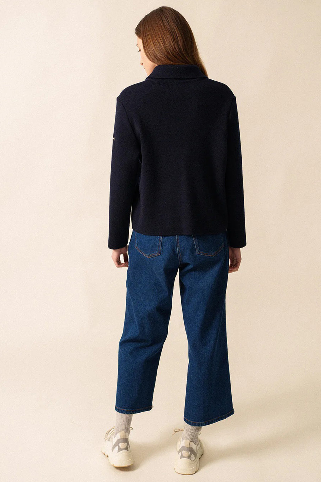 Person wearing a navy sweater and blue jeans on a beige background