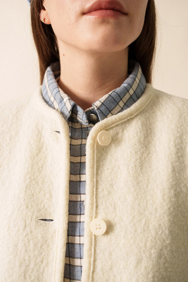 Close-up of a person wearing a cream-colored coat with a plaid shirt underneath.