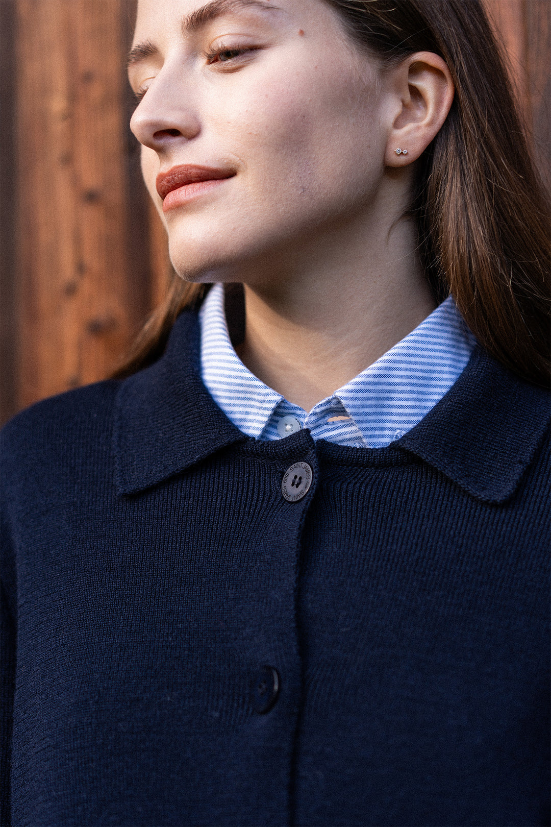 Person wearing a navy blue coat with a striped shirt underneath, against a wooden background.