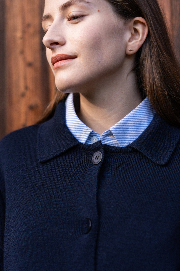 Person wearing a navy blue coat with a striped shirt underneath, against a wooden background.