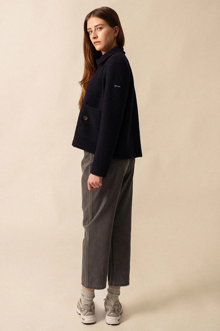 Woman wearing a black coat and gray pants on a beige background